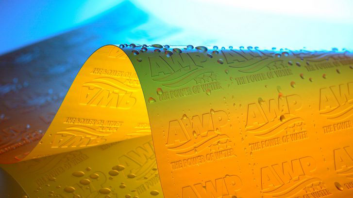 Close-up of a flexible yellow sheet embossed with "AWP" and "The Power of Water," covered with water droplets and illuminated by blue and white light.