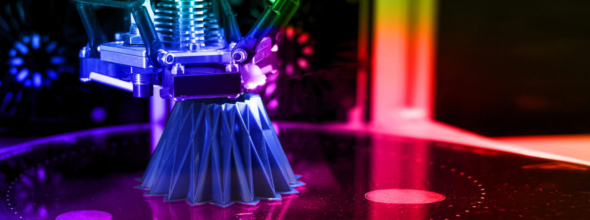 A 3D printer creates a geometric object with a textured surface, illuminated by colorful lighting in a modern workspace.