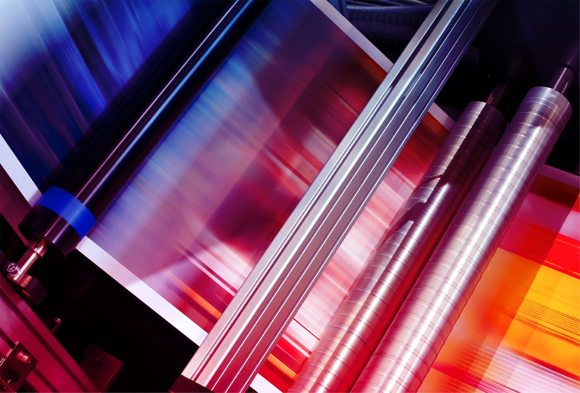 Close-up view of a printing press in operation, showing rollers and a sheet of paper with colorful printed patterns.