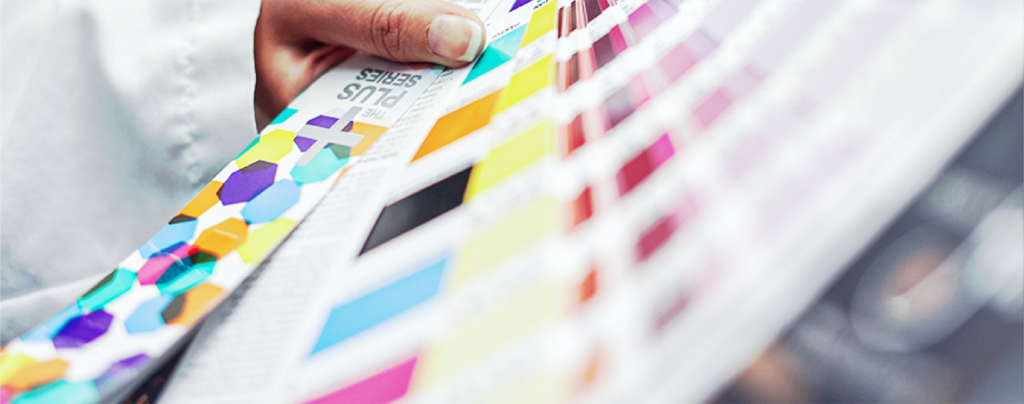 A hand holds a color swatch book with various color samples and geometric patterns visible on the pages.