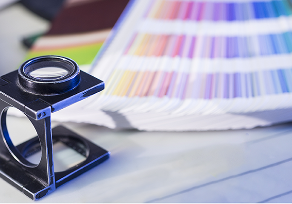 A magnifying glass sits on a table next to an open color swatch book displaying various shades.