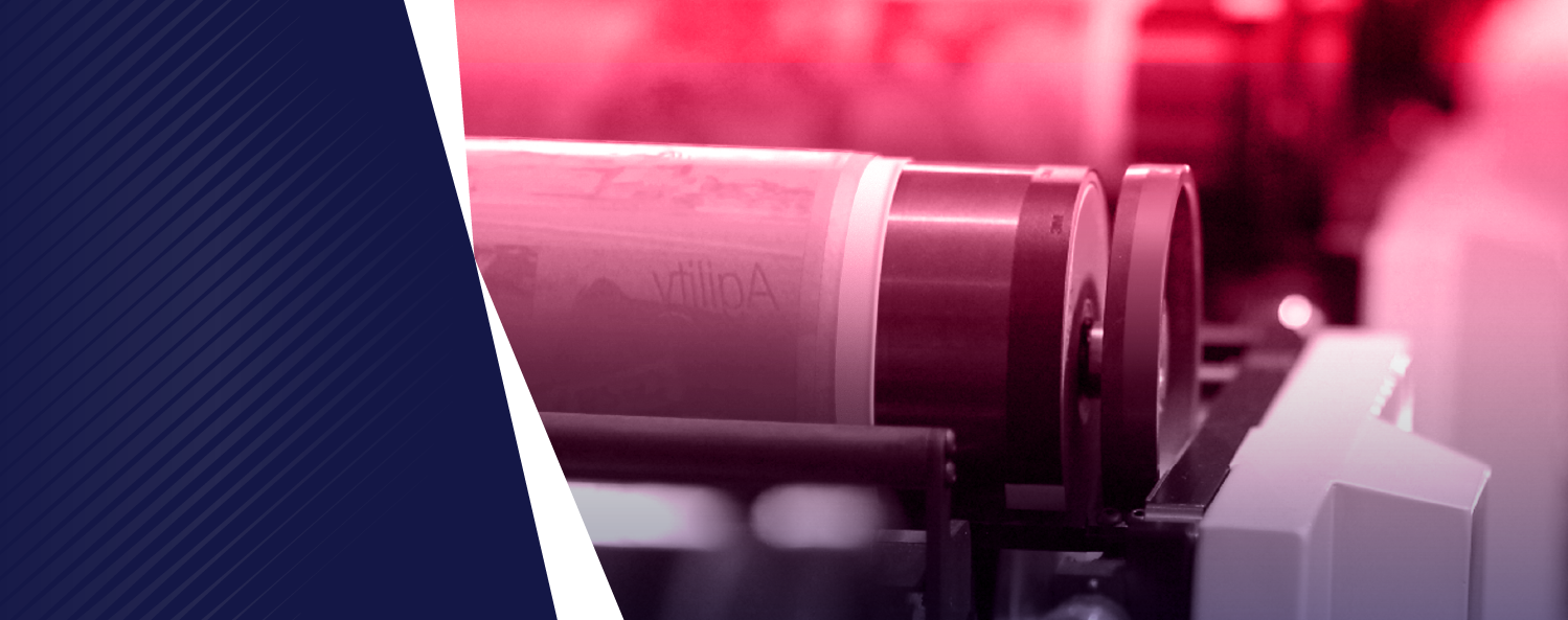 Close-up of an industrial printing press roller with a pinkish-red light in the background and a dark blue diagonal stripe on the left.