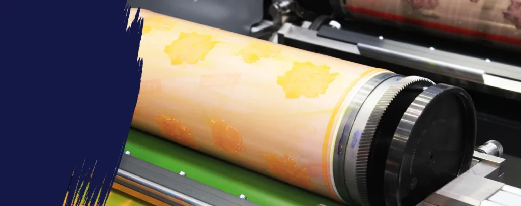 Close-up of a printing press roller with a yellow patterned design, partially obscured by a dark blue paint stroke on the left side.