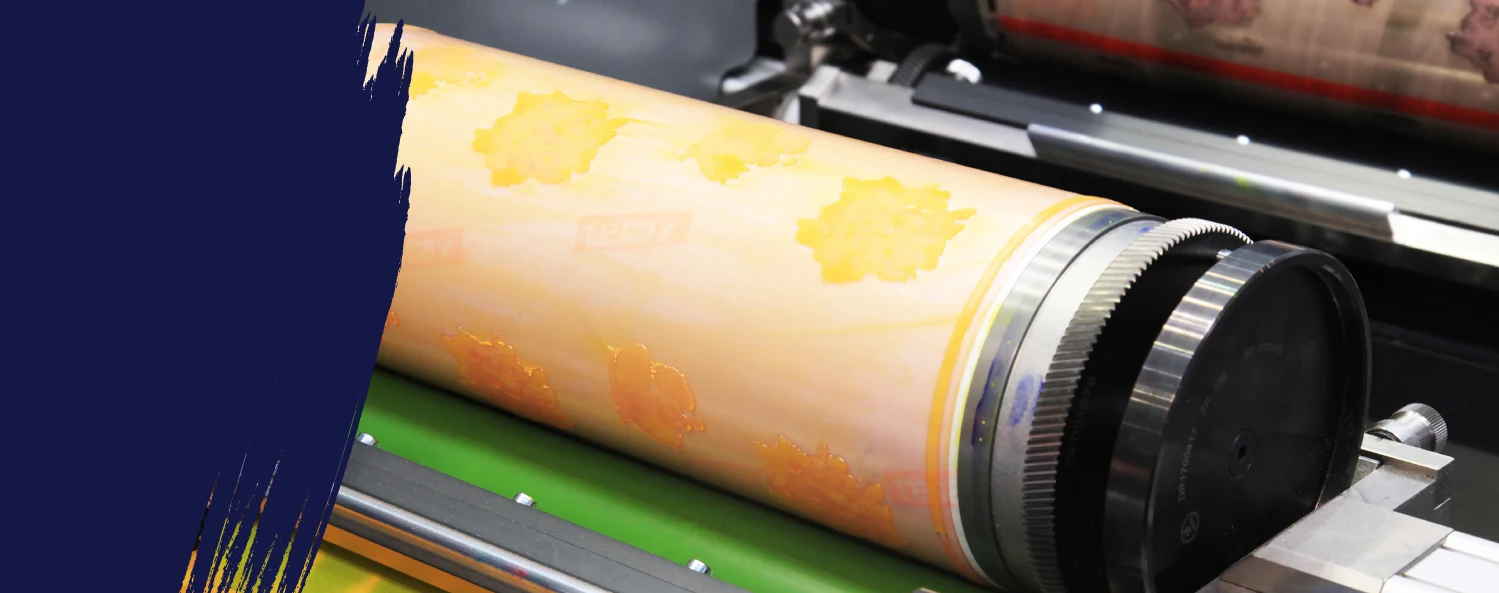 Close-up of a printing press roller with a yellow patterned design, partially obscured by a dark blue paint stroke on the left side.