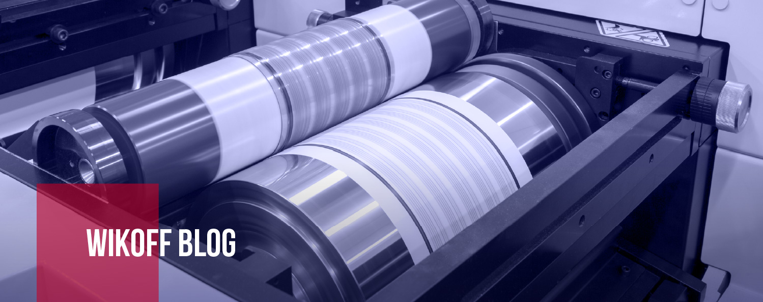 Close-up of a printing press roller with metallic parts, featuring the text "Wikoff Blog" in a red box on the lower left corner.