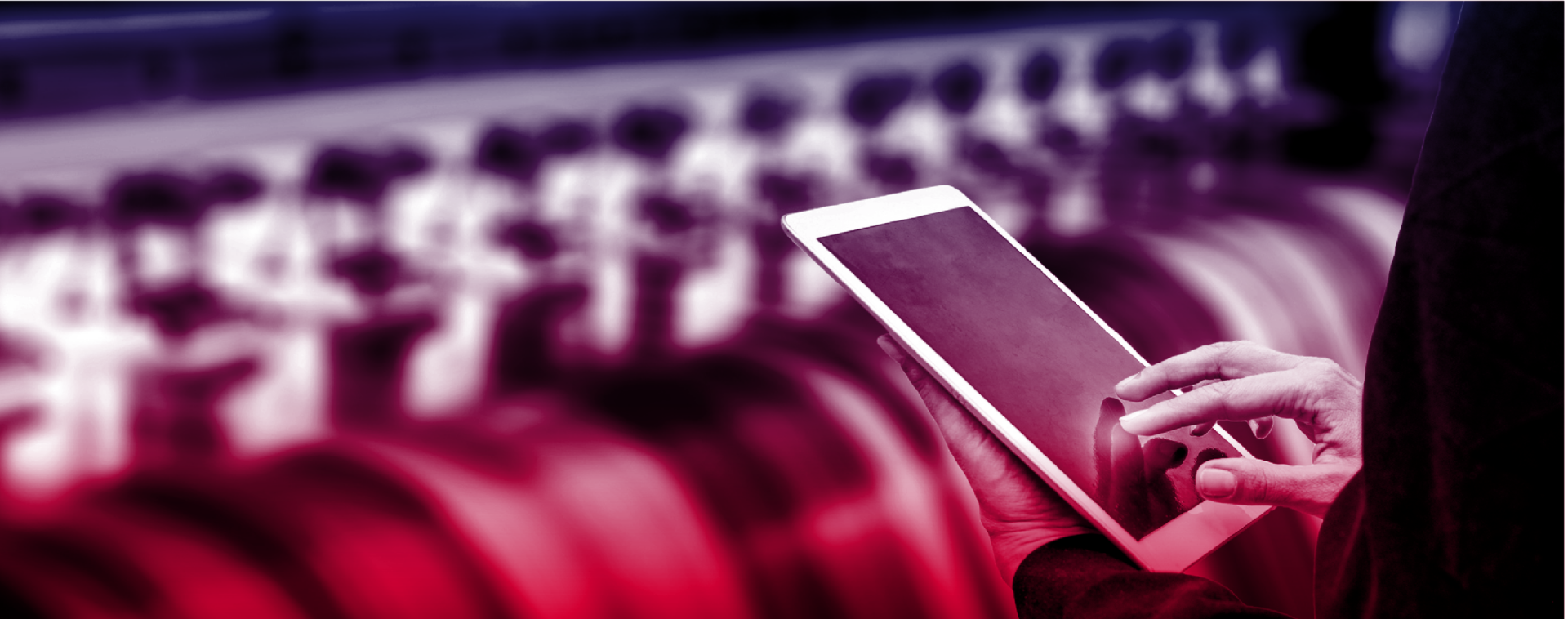 A person uses a tablet in front of industrial machinery with a blurred background, showing interaction with technology in a manufacturing or industrial setting.