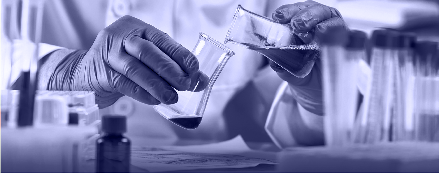 Person in lab coat and gloves pouring liquid from one beaker to another, surrounded by laboratory glassware and equipment.
