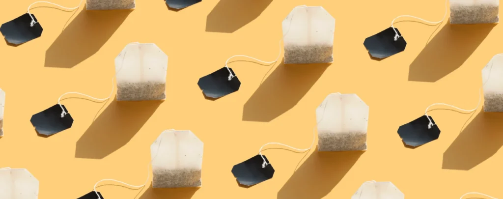 Multiple tea bags with white pouches and black tags arranged in a repeating pattern on a yellow background.