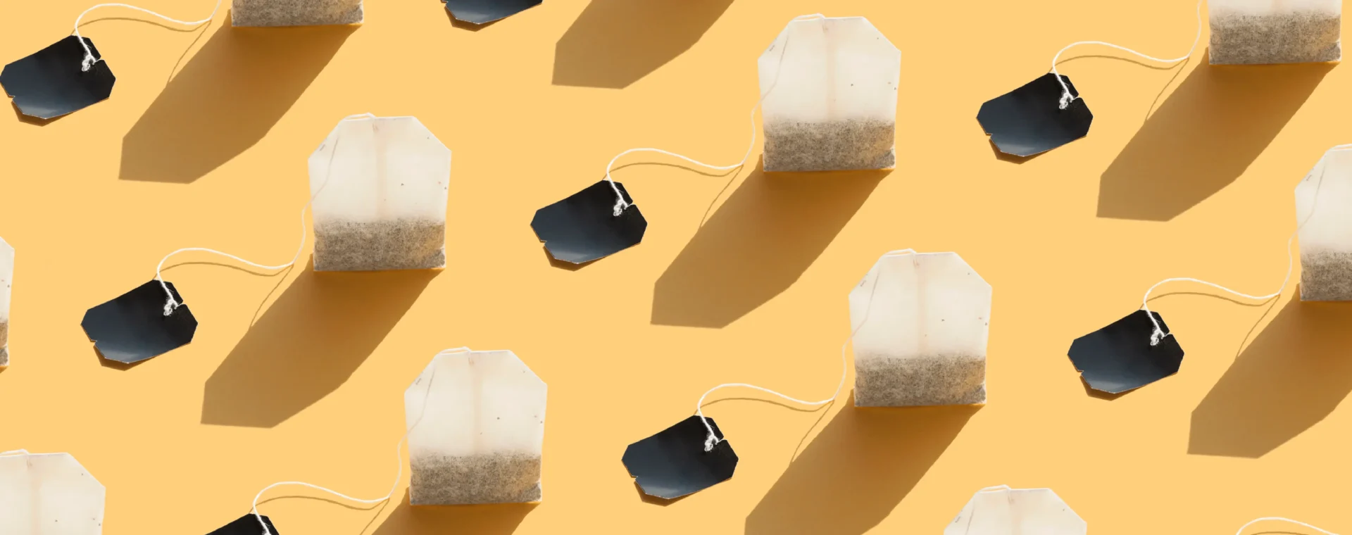 Multiple tea bags with white pouches and black tags arranged in a repeating pattern on a yellow background.
