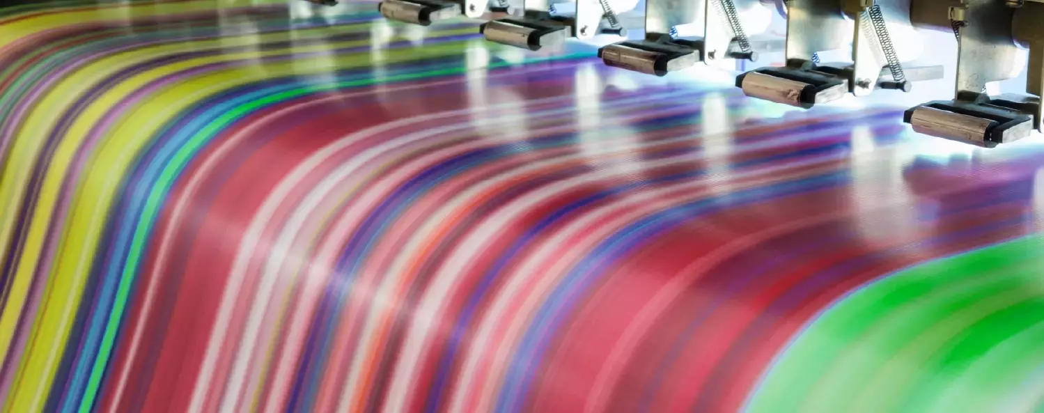 Close-up of a digital printer producing a multicolored, striped pattern on paper or fabric, with vivid colors and printing heads visible above.