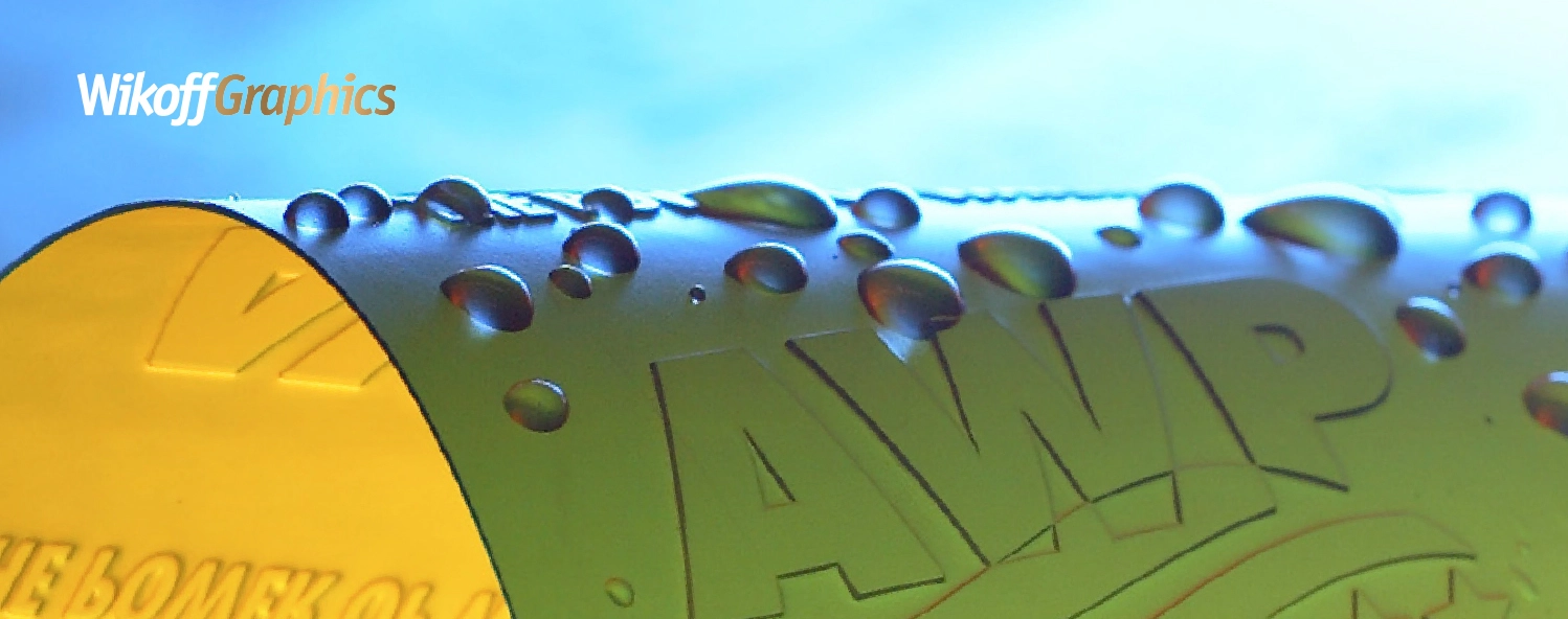 A close-up of a cylindrical object labeled "AWP" with water droplets on its surface; the Wikoff Graphics logo appears in the top left corner.