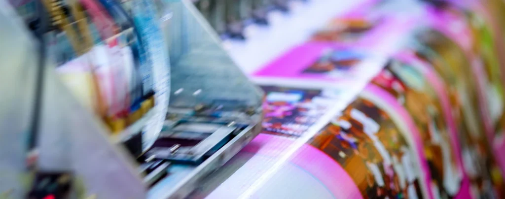 Close-up of a printing press producing colorful, glossy pages with blurred motion, showing vibrant magenta and other colors.
