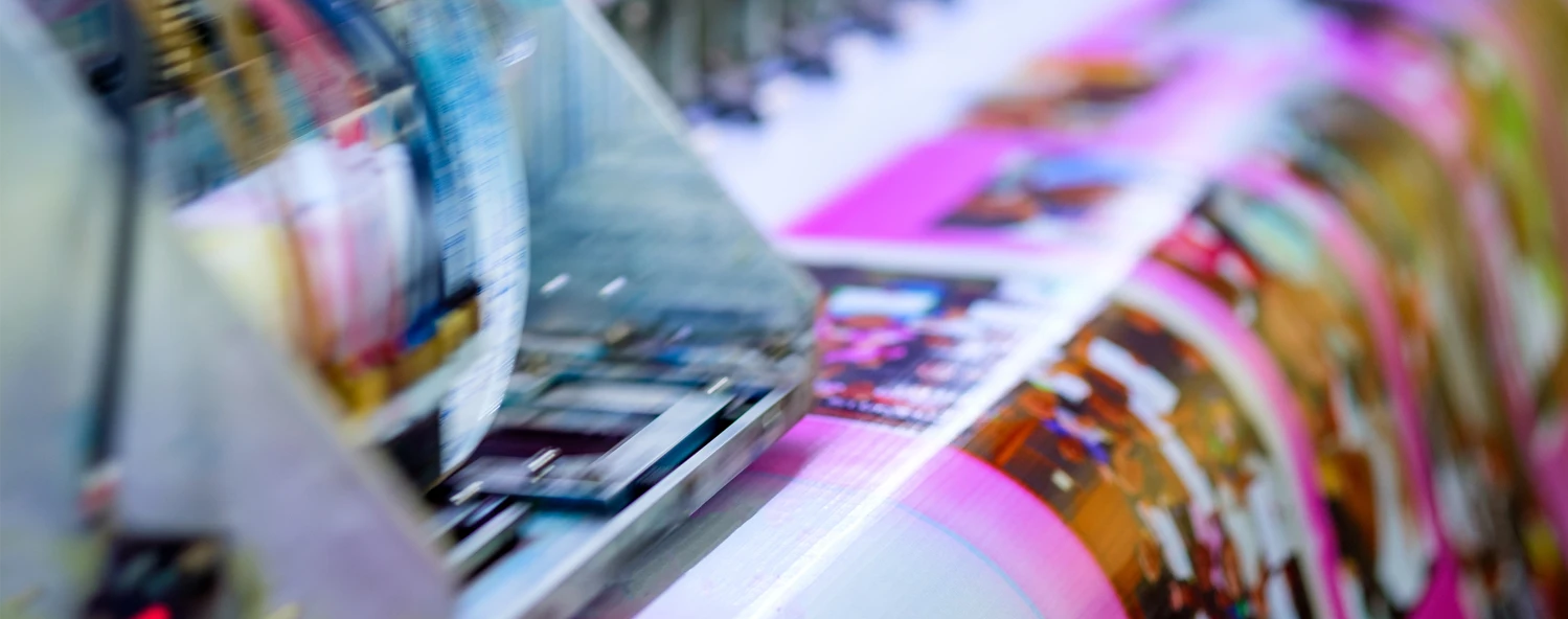 Close-up of a printing press producing colorful, glossy pages with blurred motion, showing vibrant magenta and other colors.