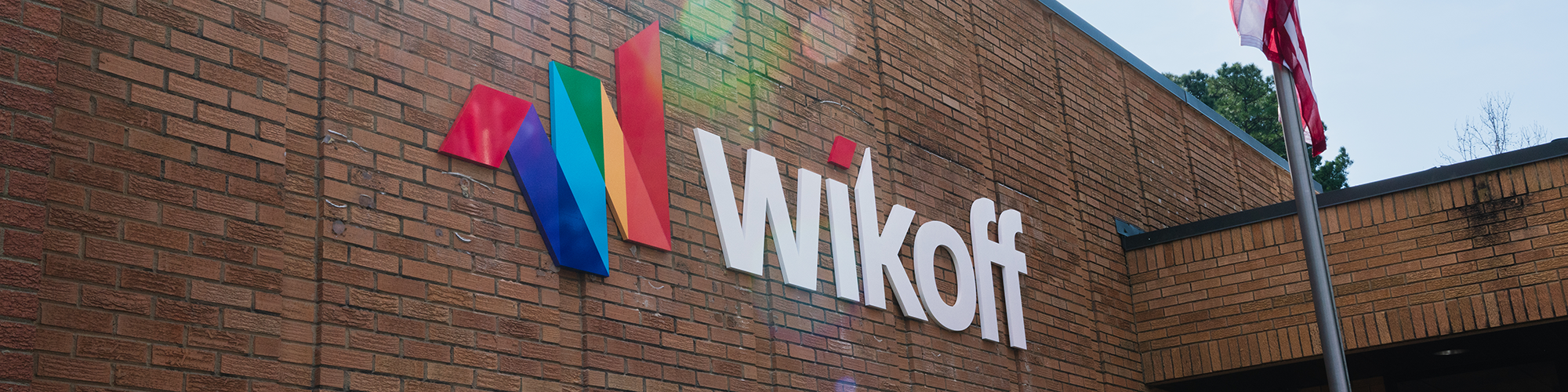 The brick exterior of a building features the Wikoff logo with colorful geometric shapes and white letters; a flagpole is visible on the right.