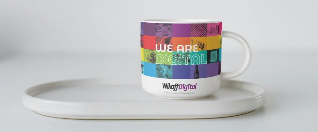 A white mug with a colorful rainbow grid and the text "We Are Digital" above the "WikaDigital" logo, placed on a white tray.