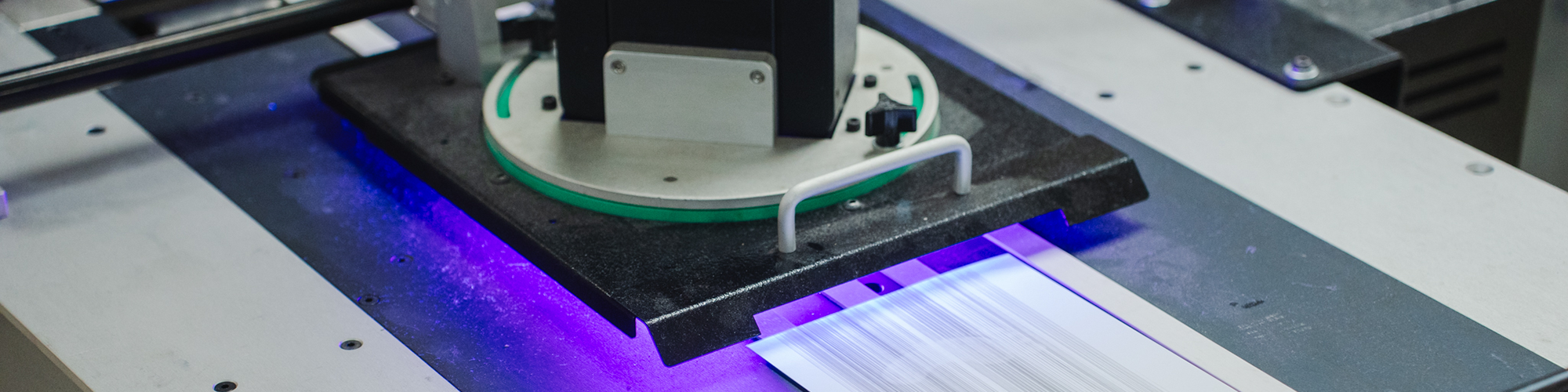 Close-up of an industrial printer or scanner processing a sheet of paper, with a blue light illuminating the paper as it moves through the machine.