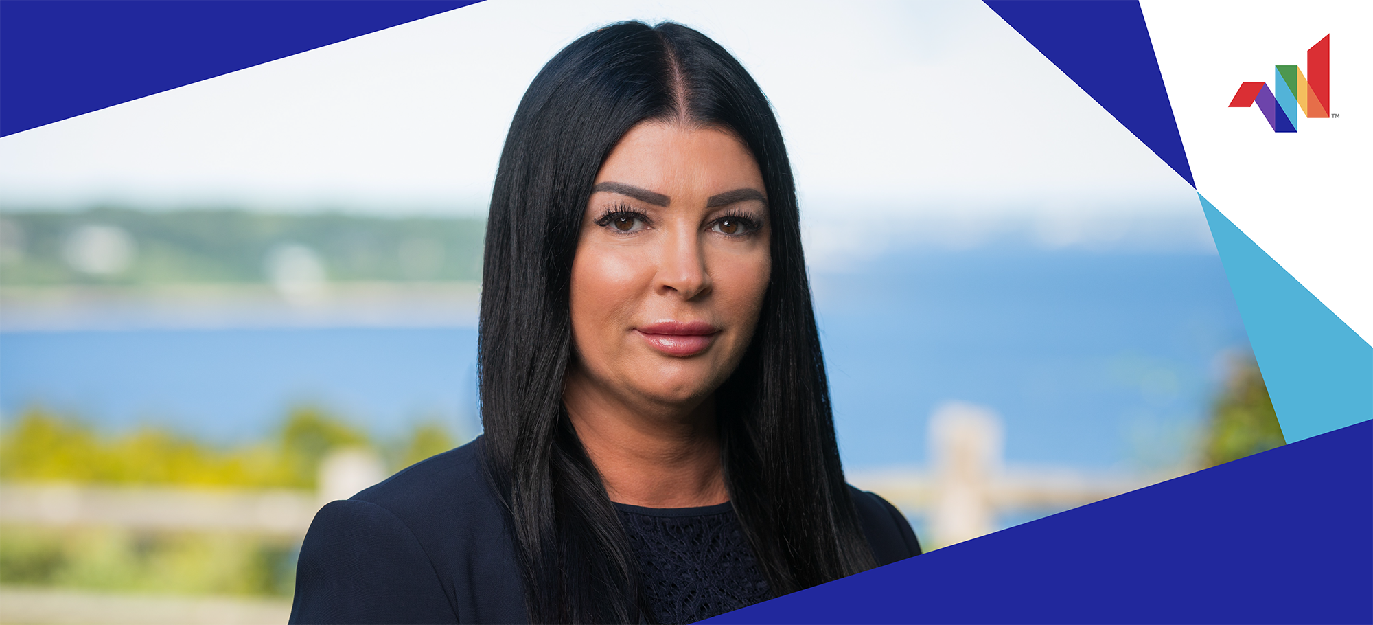 Woman with long dark hair in a navy blazer stands outdoors with a blurred background of water and greenery; geometric blue and white shapes frame the image, with a multicolor logo in the corner.