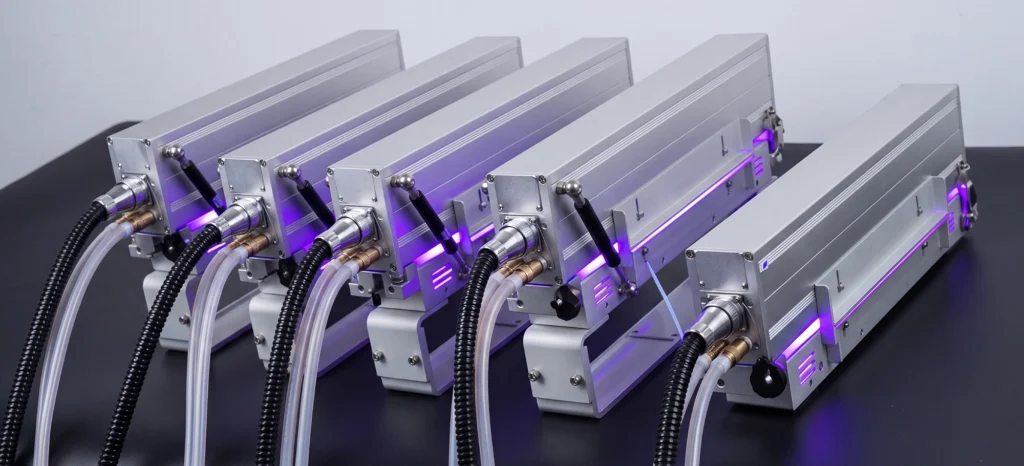 Five industrial metallic devices with attached tubes and cables are arranged in a row on a black surface, illuminated by purple LED lights.