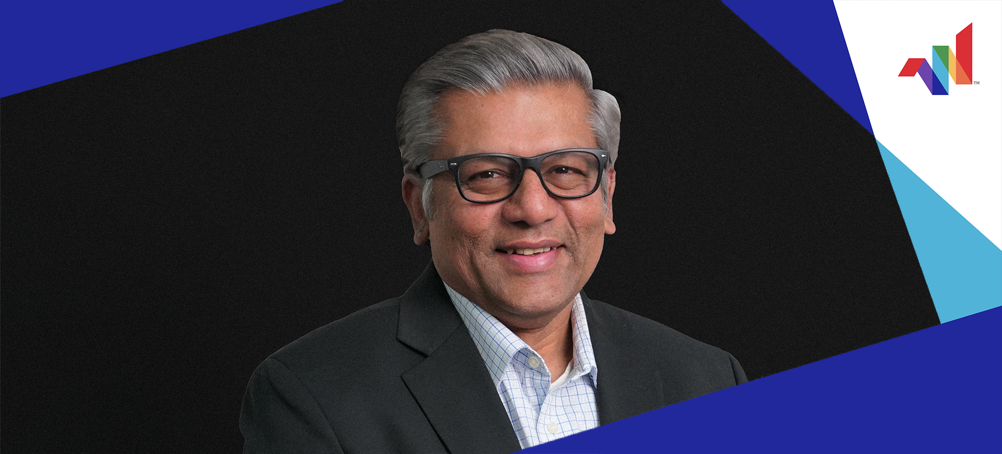 Smiling man with gray hair and glasses in a blazer, posed against a black background with geometric blue and white shapes and a multicolored logo in the corner.
